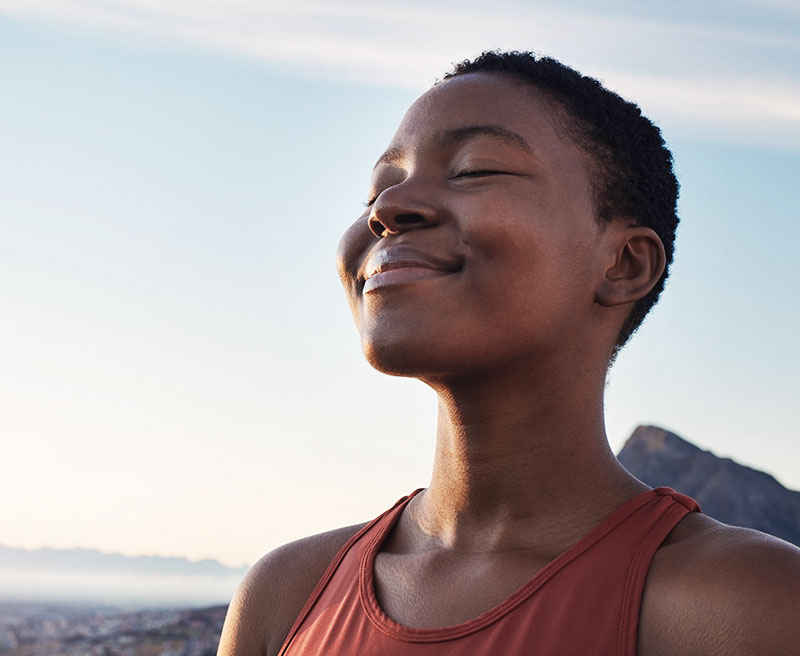 A woman in a pink tank top smiling and taking a break while out on a run in the mountains